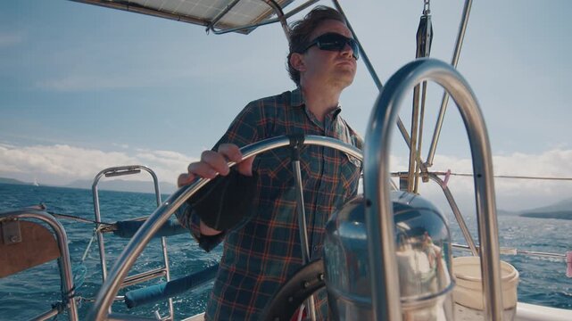 Young man sailor sailing alone the small sailing boat in the fresh sea during nice sunny day. Sailor enjoys the wind. Confident sailor steers the sail boat