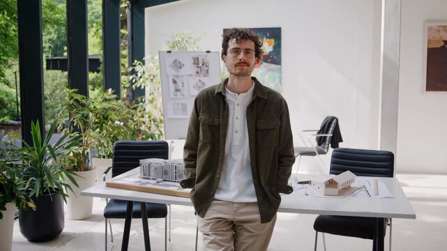 Confident bearded man designer in glasses leans on desk in office