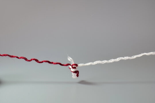Red and white threads tied together with a knot. Minimal concept of connection, unity, relationships, trust, problem solving, and strong bonds