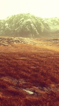 A wide grass field meets a mountain range under a cloudy sky. The daylight fades as the sun sets. The horizon shows the outline of the mountains.