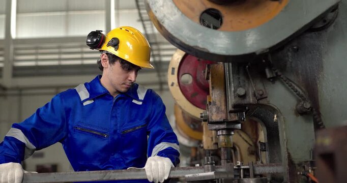 Factory worker operating power press machine to stamp metal bar in manufacturing plant