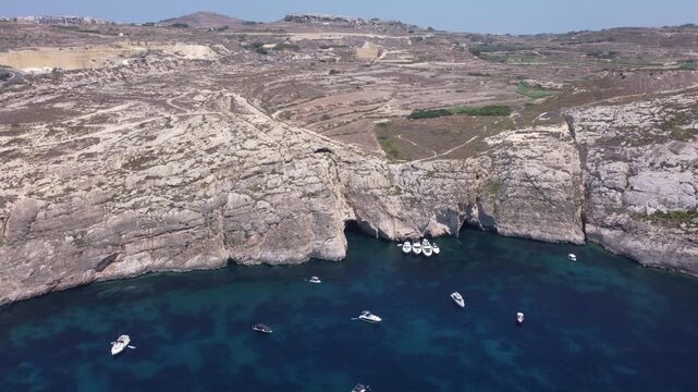 Aerial view of the rugged limestone cliffs of Dwejra Bay with deep blue Mediterranean waters under a clear sky in Gozo region, Malta. High quality 4k footage
