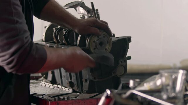 Close up view of a mechanic assembly or repairing an internal combustion engine block with hands in a workshop. Industrial mechanical maintenance service. Metallic automotive part on a workbench.