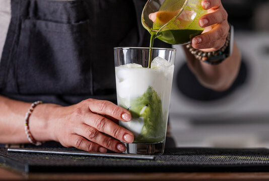 Woman Bartender Pouring Matcha Tea Into Glass With Milk And Ice