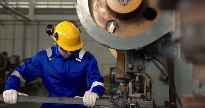 Factory worker operating power press machine to stamp metal bar in manufacturing plant