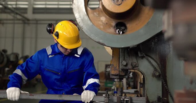 Factory worker operating power press machine to stamp metal bar in manufacturing plant