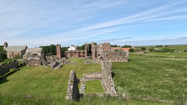 Pull-back shot of historic abbey ruins set in lush green grass swaying in the wind under bright sunshine, revealing a wider peaceful countryside landscape.