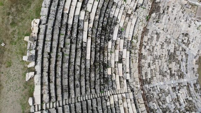 A cinematic upward vertical drone movement starting from a close-up texture of ancient Roman theater stone seats (cavea) and rising smoothly to reveal the grand scale of the entire historic amphitheat