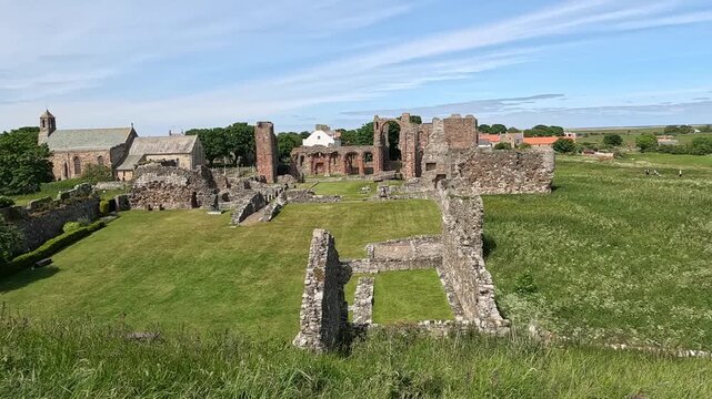 Panning shot over historic abbey ruins surrounded by lush green grass swaying in the wind under bright sunshine, sweeping across the peaceful ancient landscape.