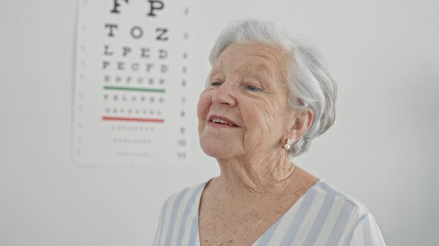 Woman senior patient holding glasses during eye test in optometry clinic, gazing at the eye chart on the wall; vision check calm.