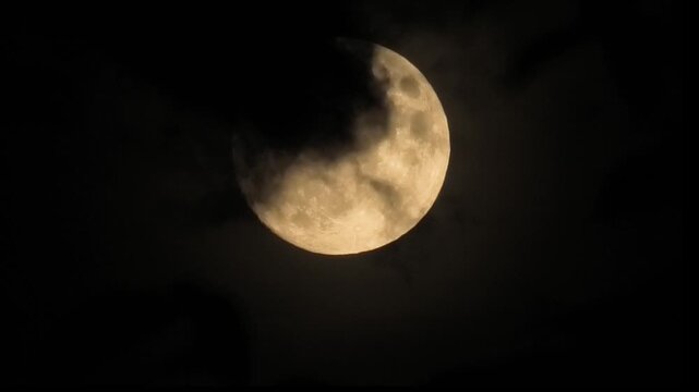 The full moon hides behind dark clouds in the night sky. A close-up shot of a supermoon, captured with a telephoto lens