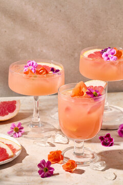Three glasses of refreshing summer cocktails with grapefruit slcies and edible flowers