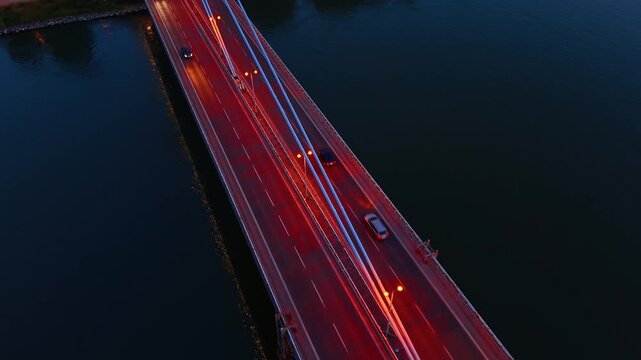 Panoramic view of SNP Bridge over the Danube river. A red articulated bus crosses a multi lane highway near large passenger ships at sunset in Bratislava.