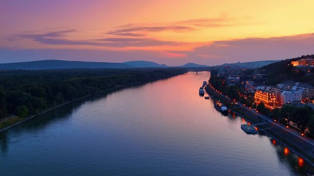 Danube river at vibrant sunset in Bratislava Slovakia. Aerial view of river water under colorful evening sky with city embankment and distant hills.