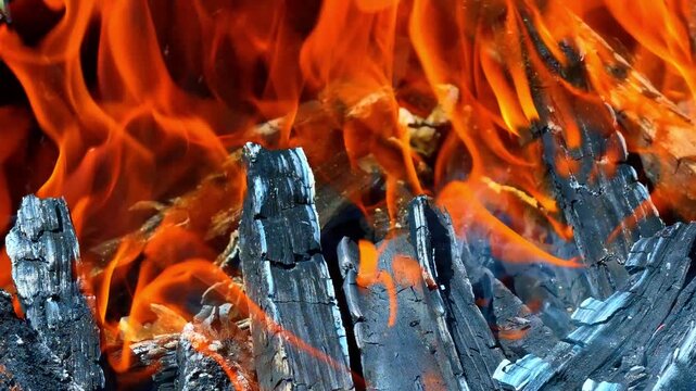 Burning logs with bright orange flames close up. Charcoal wood texture under active hot yellow fire in a grill