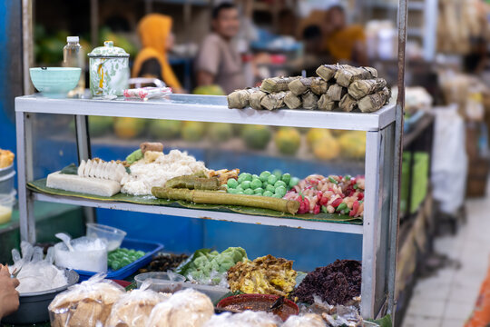 An assortment of traditional Javanese sweet snacks (lenjongan), including cenil, klepon, gethuk, and grontol, displayed on banana leaves inside a glass display cabinet at Pasar Gede, Solo.