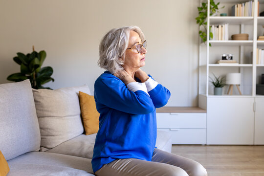 Senior woman suffering from neck pain while sitting on sofa at home