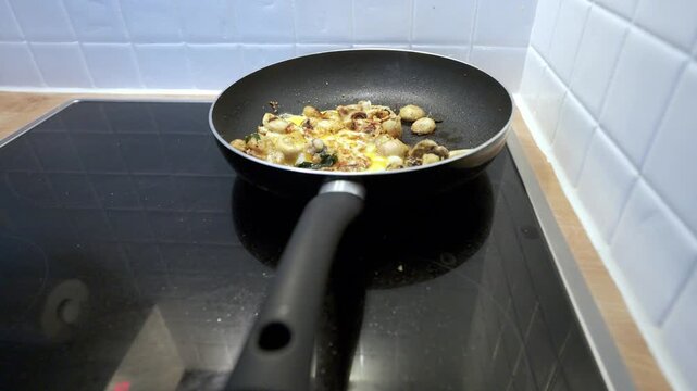 Frying scrambled eggs with champignon mushrooms and spices in a pan on a modern induction cooktop