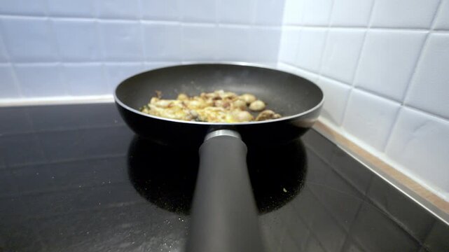 Delicious scrambled eggs with mushrooms and greens frying in a hot pan on an induction cooktop