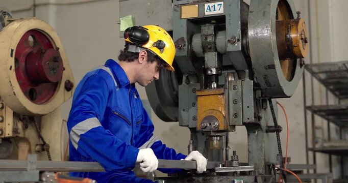 Factory worker operating power press machine to stamp metal bar in manufacturing plant