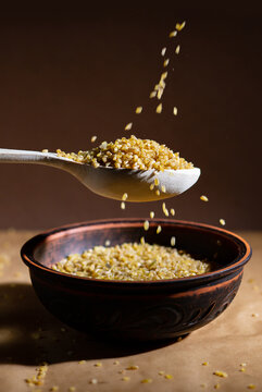 Raw Bulgur Falling into Rustic Ceramic Bowl