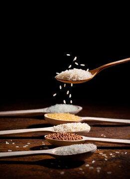 Raw White Rice Falling from Wooden Spoon on Dark Background