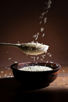 Wooden Spoon with Raw Long Grain Rice over Rustic Ceramic Bowl