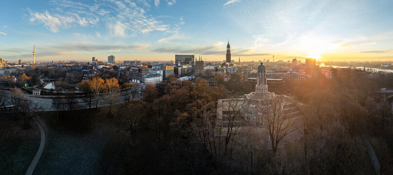Aerial view of the Bismarck Monument in a park with the city skyline, church spires, and sunrise in the background in Hamburg, Hamburg, Germany.