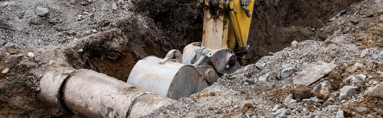 Excavator digging a trench narrow ditch in the dirt to work on underground utilities, municipal construction project, old concrete pipe exposed  © knelson20