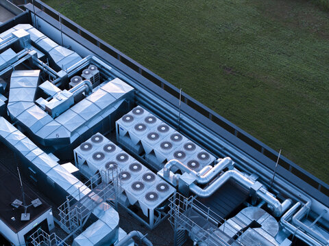 Aerial view of the industrial rooftop of a modern data center featuring rows of cooling fans and metallic ventilation ducts adjacent to a green area in Krakow, Lesser Poland Voivode, Poland.