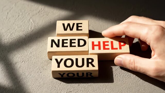 A human hand places a wooden block spelling HELP next to other letter blocks