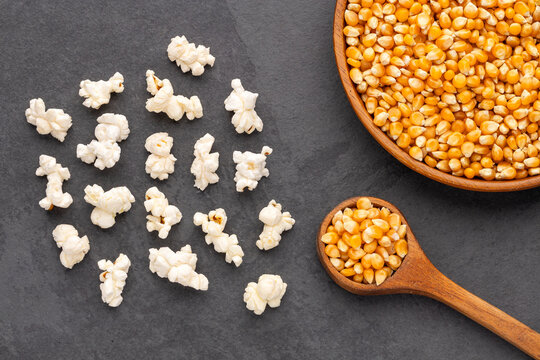 Composition with white popcorn and popping corn on a black stone surface, with space for text.