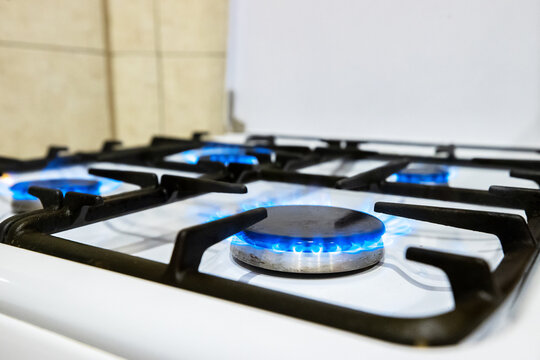 Blue gas flames burning on a white stove with black cast iron grates indoors. Kitchen appliance