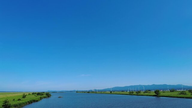 【4K】津軽大橋から望む岩木川と遠く広がる小泊岬：初夏の青空と瑞々しい緑。青森の豊かな大自然を捉えたランドスケープ移動映像素材　[4K] Scenic View of Iwaki River and Distant Cape Kodomari from Tsugaru Bridge: Summer Landscape in Aomori Japan 撮影日：20260624-1

