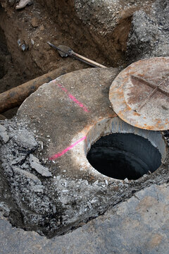 Underground utilities construction project, precast concrete stormwater system access vault in dirt trench under road, old iron pipe, shovel and tamper bar
