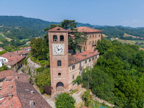 Aerial view of the historic brick clock tower and castle complex surrounded by lush green hills and terracotta rooftops in Casalborgone, Piedmont, Italy.