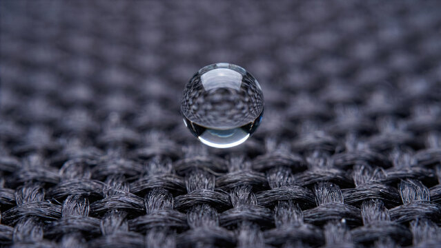 Extreme macro of thick transparent water drop forming perfect sphere on dark waterproof fabric