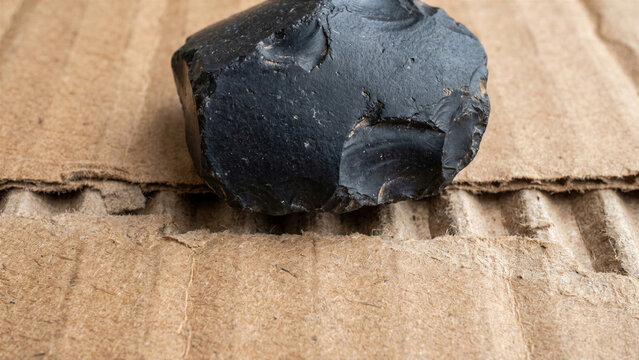Macro view of single piece of dark unpolished obsidian stone on sheet of corrugated cardboard