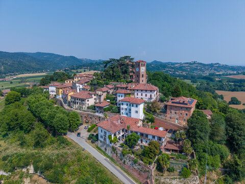 Aerial view of the historic village of Casalborgone featuring traditional terracotta rooftops, a prominent clock tower, and surrounding lush green hills in Casalborgone, Piedmont, Italy.