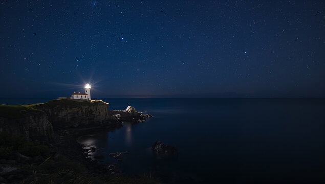 満天の星の下で暗い海を照らす断崖の灯台