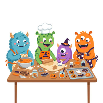 Cute monsters baking Halloween cookies together on a wooden table