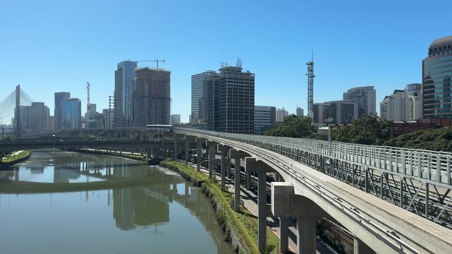 Modern elevated monorail traveling above an urban river with skyscrapers in the background