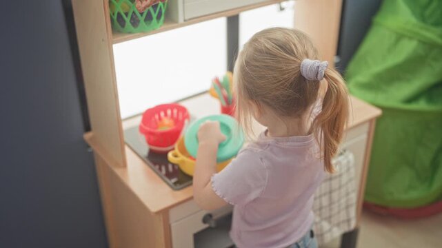 Girl holds a green plastic plate and stirs with hand over a toy pot while playing at a play kitchen in a building; playfulness imagination.