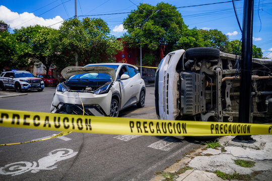 Urban traffic accident scene in Mexico featuring a damaged electric car and a commercial van completely overturned on its side