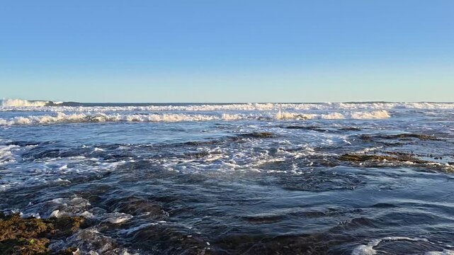 Static Shot Of Ocean Waves Rolling In the Backgroud With Small Waves Flowing Through Gaps In a Roky Shore Covered In Orange Seaweed