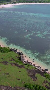 Aerial seascape turquoise bay with cliffs overlooking verdant grassy slopes, clear shallow reef patches,Bukit Merese, Lombok, Tanjung Ann, Indonesia,vertical video