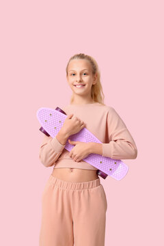 Happy teenager girl with skateboard on pink background