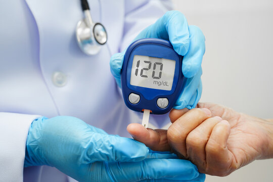 Asian doctor using digital glucose meter for check sample blood sugar level to treatment diabetes.