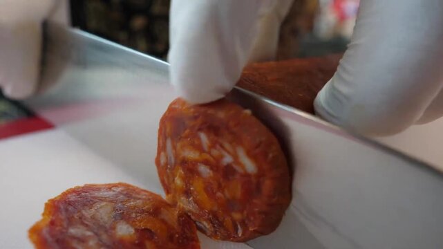 close-up footage of a sharp knife slicing a fresh, vibrant Italian chorizo sausage on a white cutting board. The shot highlights the rich red texture, marbled fat, and spicy seasoning of the meat, ide