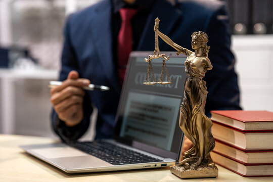 Lawyer in a suit working at a desk with a laptop, justice statue, pen and stacked books in a legal office